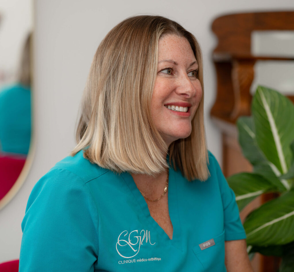 Portrait de Geneviève, propriétaire de la Clinique médico esthétique CGM, souriante et vêtue de l’uniforme turquoise de la clinique, dans un décor chaleureux et lumineux