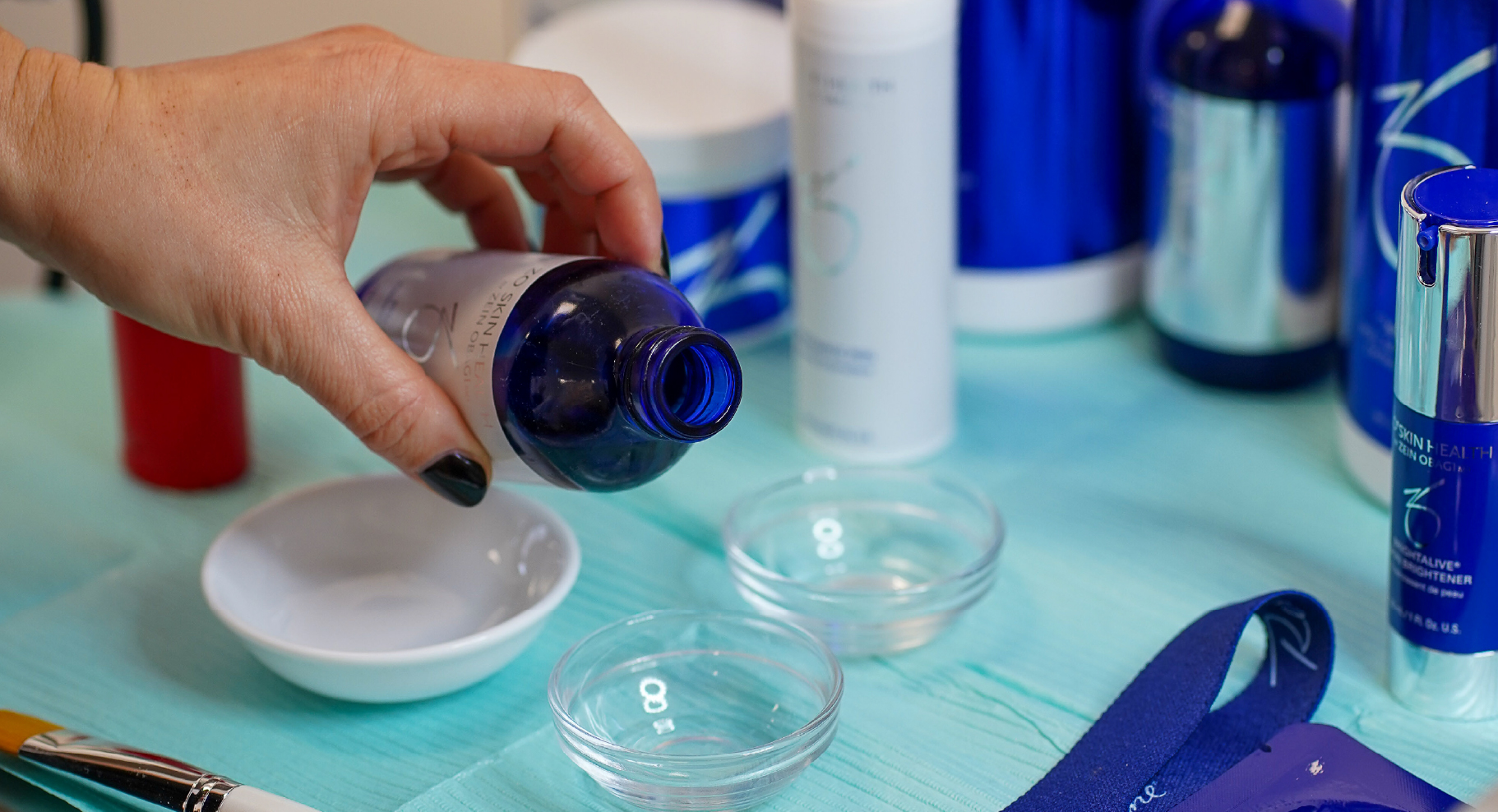Application d’un soin ZO Skin Health avec une main qui verse une solution dans une coupelle en verre entourée de produits professionnels de la marque