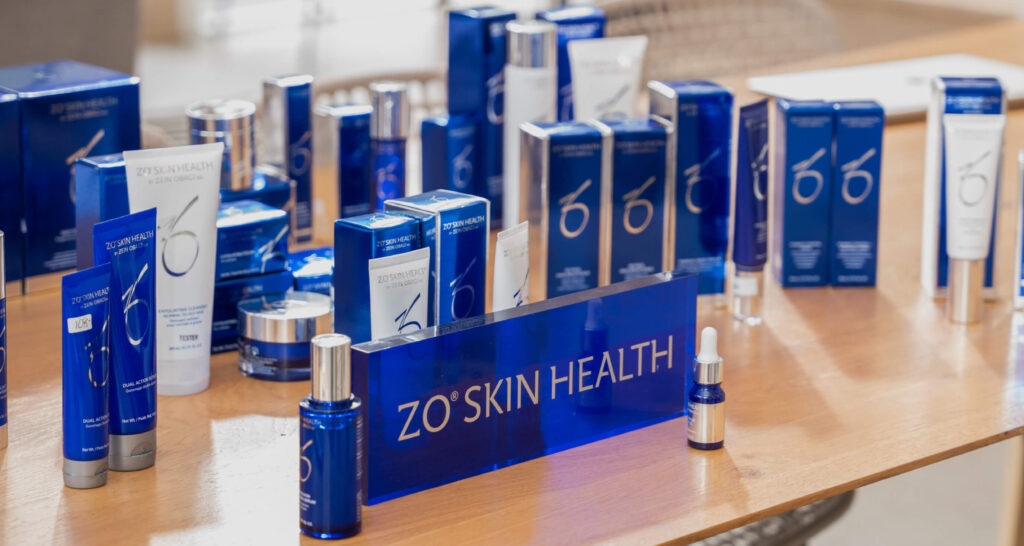 Gamme complète de soins de la peau ZO Skin Health exposée sur une table, incluant nettoyants, sérums, crèmes et protections solaires en emballages bleu et argent